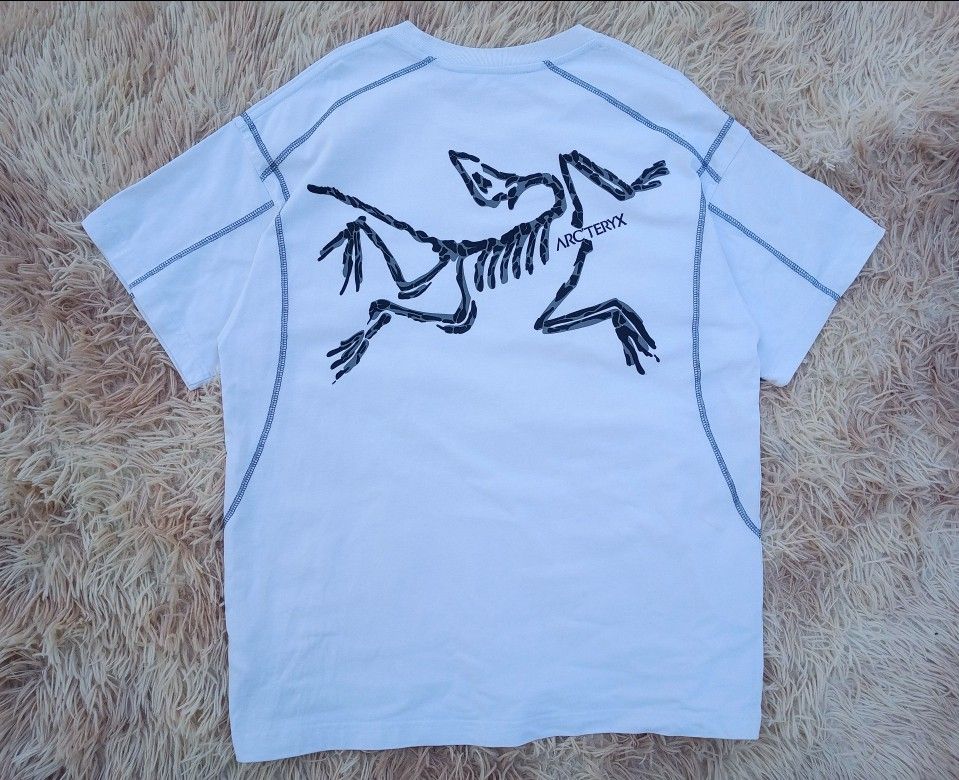 Arc'teryx White T-Shirt with Skeleton Logo (Category: Tshirts & Polo Shirts ) located in Boston. Submitted by johnpaulvi30029 (Listing ID 1461277592, Image 1). Description: - White Arc'teryx T-shirt - Size: Medium (M) - Iconic skeleton logo graphic on back - Smaller logo on front - Contrasting stitching details along seams - Made in China - Perfect for casual wear.