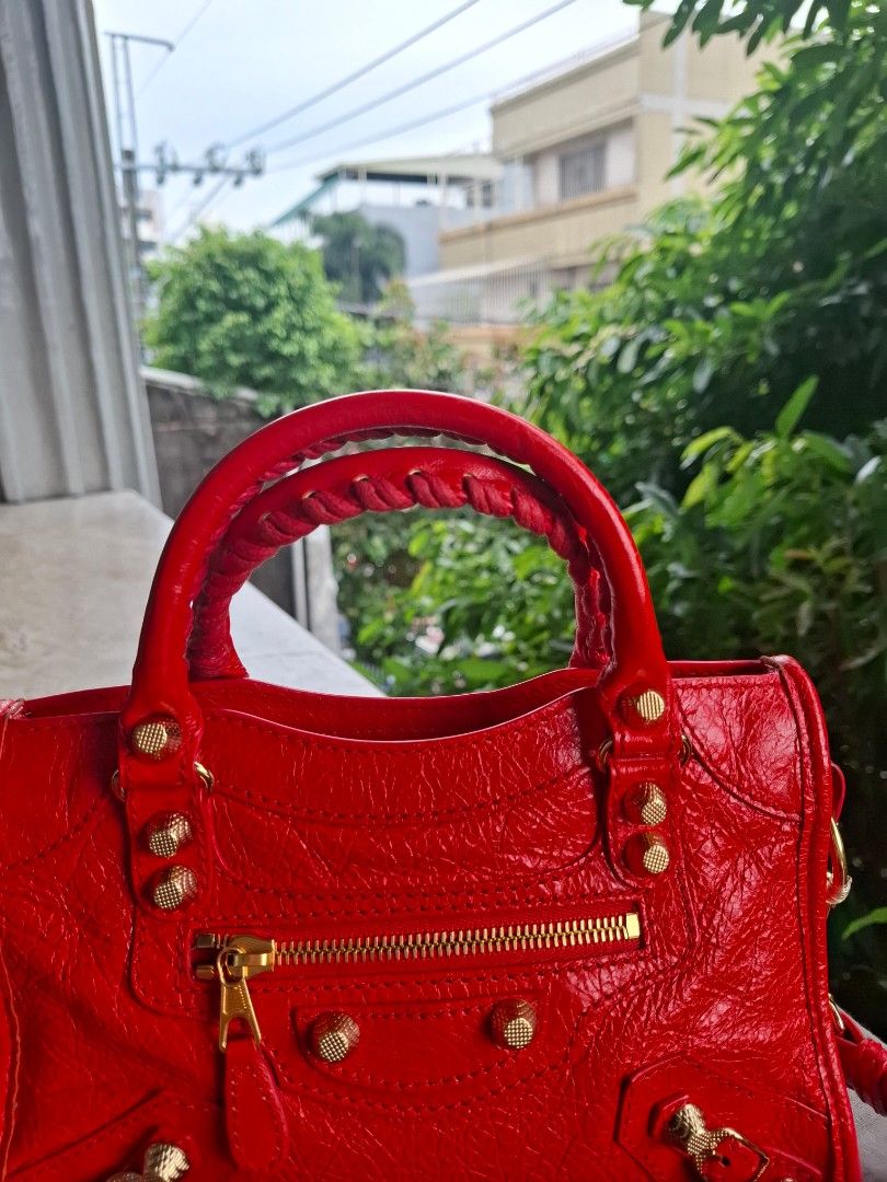 Authentic Balenciaga City Mini (Category: Luxury Bags & Wallets) located in Del Monte. Submitted by silvertree_520244 (Listing ID 1461196498, Image 3). Description: - Authentic red orange leather Balenciaga City bag - Features classic studs and zip details - Comes with the signature Balenciaga mirror and long strap - Soft, slouchy leather with sturdy handles.