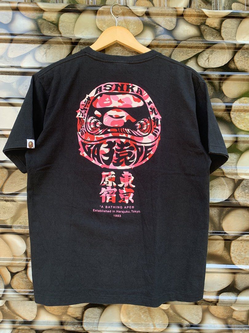 BAPE A Bathing Ape Daruma Graphic Tee (Category: Tshirts & Polo Shirts ) located in Aloran. Submitted by chester78864 (Listing ID 1461285552, Image 1). Description: - Brand: A Bathing Ape (BAPE) - Color: Black - Size: Medium (M) - Design: Features a cool Daruma graphic on the back. - Front Details: A Bathing Ape logo and "Tokyo Harajuku" text. - Ideal for: Streetwear fans and collectors..