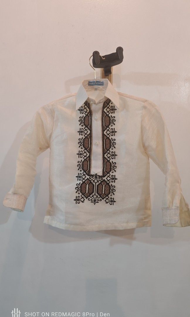 Barong for Kids (Category: Babies & Kids Fashion) located in Manila. Submitted by dentoters (Listing ID 1461135508, Image 1). Description: Measurements: Length - 40cm Width (shoulders) - 30cm Sleeve length - 38cm Description: - Cream-colored Barong Tagalog shirt for boys age 3-4 years old. Features intricate brown and black embroidery on the chest. - Long sleeves with button cuffs. Made from a light, slightly sheer fabric. Ideal for formal events