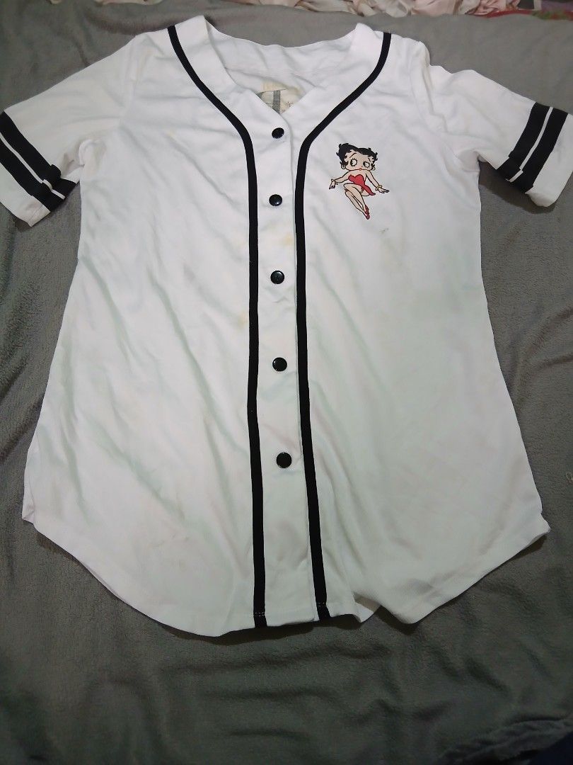 Betty Boop White Baseball Jersey (Category: Tshirts & Polo Shirts ) located in Bulacan. Submitted by esecleus (Listing ID 1461240233, Image 1). Description: - White baseball jersey featuring a Betty Boop graphic on the front and back. - Black trim accents the collar, placket, and sleeves. - Classic button-up front closure. - A fun and unique piece for any Betty Boop enthusiast..
