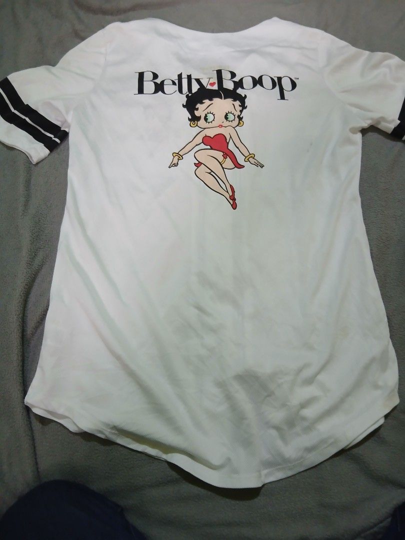 Betty Boop White Baseball Jersey (Category: Tshirts & Polo Shirts ) located in Bulacan. Submitted by esecleus (Listing ID 1461240233, Image 2). Description: - White baseball jersey featuring a Betty Boop graphic on the front and back. - Black trim accents the collar, placket, and sleeves. - Classic button-up front closure. - A fun and unique piece for any Betty Boop enthusiast..