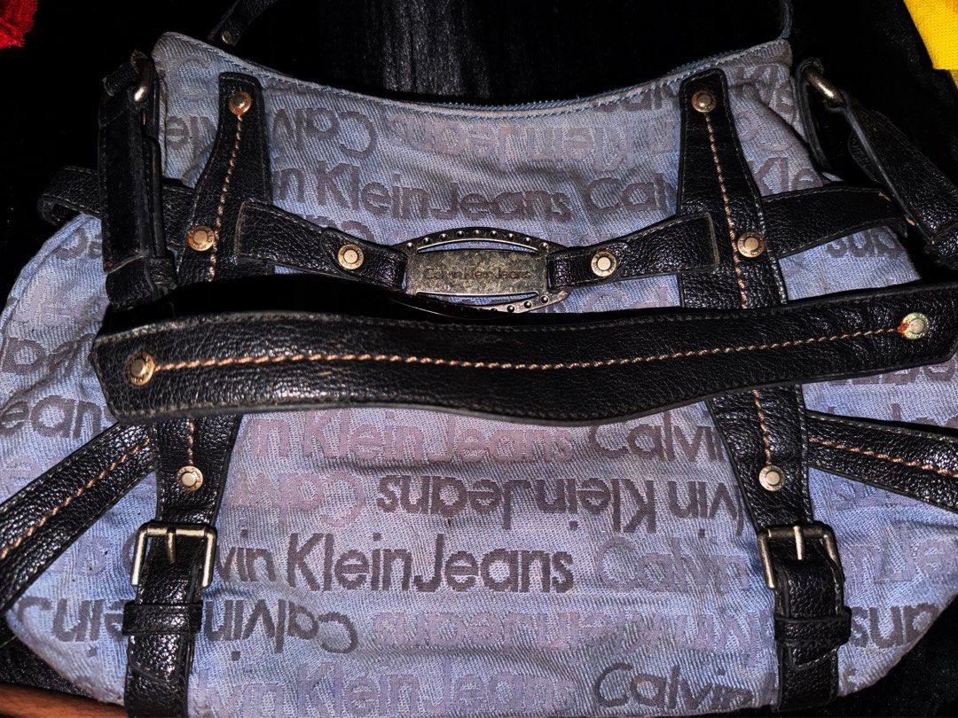 Calvin Klein Jeans Monogram Shoulder Bag (Category: Luxury Bags & Wallets) located in Cavite. Submitted by declutterringggggg (Listing ID 1461177683, Image 2). Description: - Light blue Calvin Klein Jeans shoulder bag - All-over CKJ monogram pattern - Black leather trim and straps with buckle details - Silver-tone hardware with metal logo plate - Zipper closure - Interior zippered pocket - Some signs of wear inside and out.