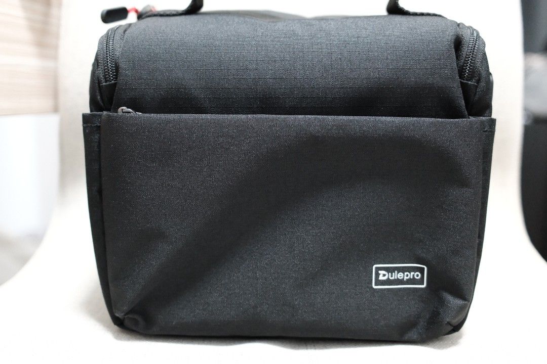 Dulepro Black Camera Bag with Handle (Category: Luxury Bags & Wallets) located in Taguig. Submitted by laluceph (Listing ID 1461144947, Image 2). Description: - Sleek black Dulepro bag - Main zippered compartment for secure storage - Convenient front pocket for quick access - Stylish red cord zipper pulls - Durable top handle for easy carrying - Perfect for carrying a small camera and accessories - Great for travel or everyday adventures.