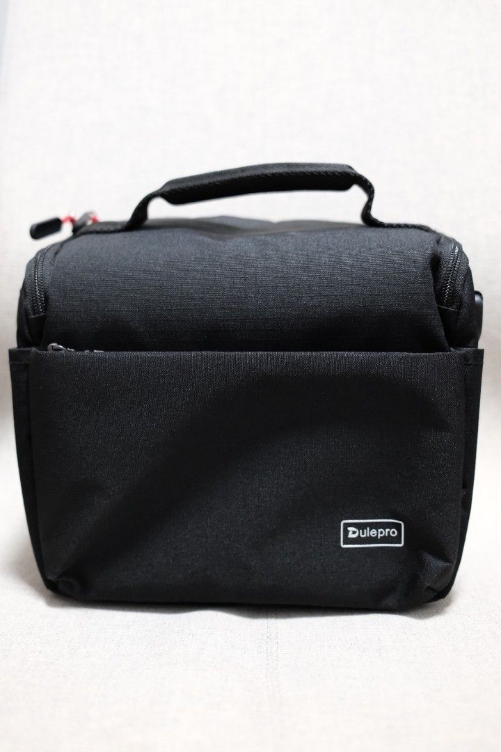 Dulepro Black Camera Bag with Handle (Category: Luxury Bags & Wallets) located in Taguig. Submitted by laluceph (Listing ID 1461144947, Image 1). Description: - Sleek black Dulepro bag - Main zippered compartment for secure storage - Convenient front pocket for quick access - Stylish red cord zipper pulls - Durable top handle for easy carrying - Perfect for carrying a small camera and accessories - Great for travel or everyday adventures.