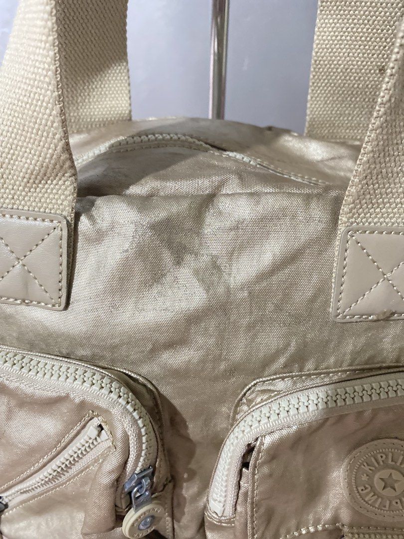 Kipling Metallic Gold Nylon Shoulder Bag (Category: Shoulder Bags) located in Tagum. Submitted by luxeukayfinds_ (Listing ID 1461208528, Image 2). Description: ‼️ CHECK EACH PHOTOS FOR SIGN OF USE‼️ - Stylish gold Kipling bag - Multiple pockets on the front for organization - Adjustable shoulder strap for comfortable carrying - Convenient top handles - Zippers are in good working condition - Ideal size for everyday essentials.