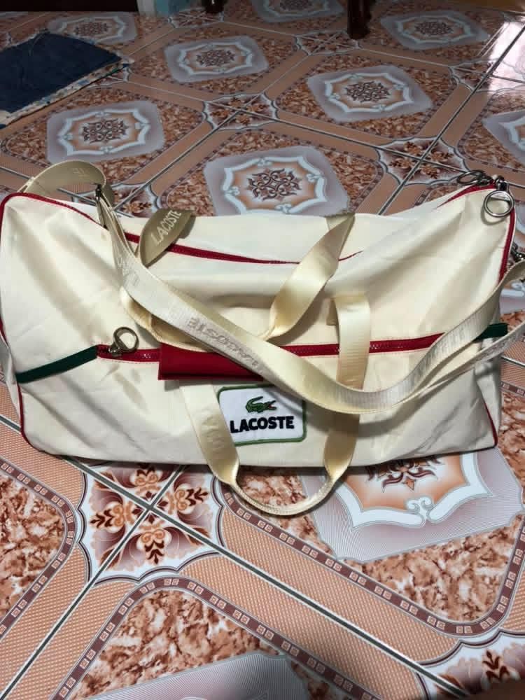 Lacoste Cream Duffel Bag (Category: Sling Bags) located in Malabon City. Submitted by matcha_frappe (Listing ID 1461261380, Image 2). Description: - Cream-colored Lacoste duffel bag - Features red and green trim details - Straps printed with 'LACOSTE' - Interior tag indicates 'Made in France' - Ideal for weekend getaways or gym sessions.