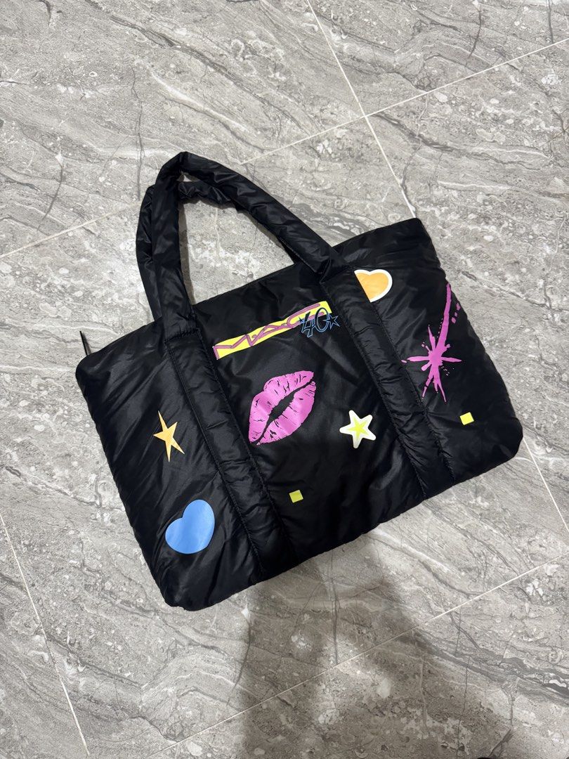 MAC Cosmetics Black Puffer Tote Bag with Graphics (Category: Tote Bags) located in Calamba. Submitted by nicalison (Listing ID 1461254647, Image 2). Description: - Chic black puffer tote bag from MAC Cosmetics. - Features playful graphics: lips, stars, and clouds. - Secure zipper closure at the top. - Comfortable, puffy handles for easy carrying. - Ideal for everyday use or travel. - Spacious interior for all your essentials..