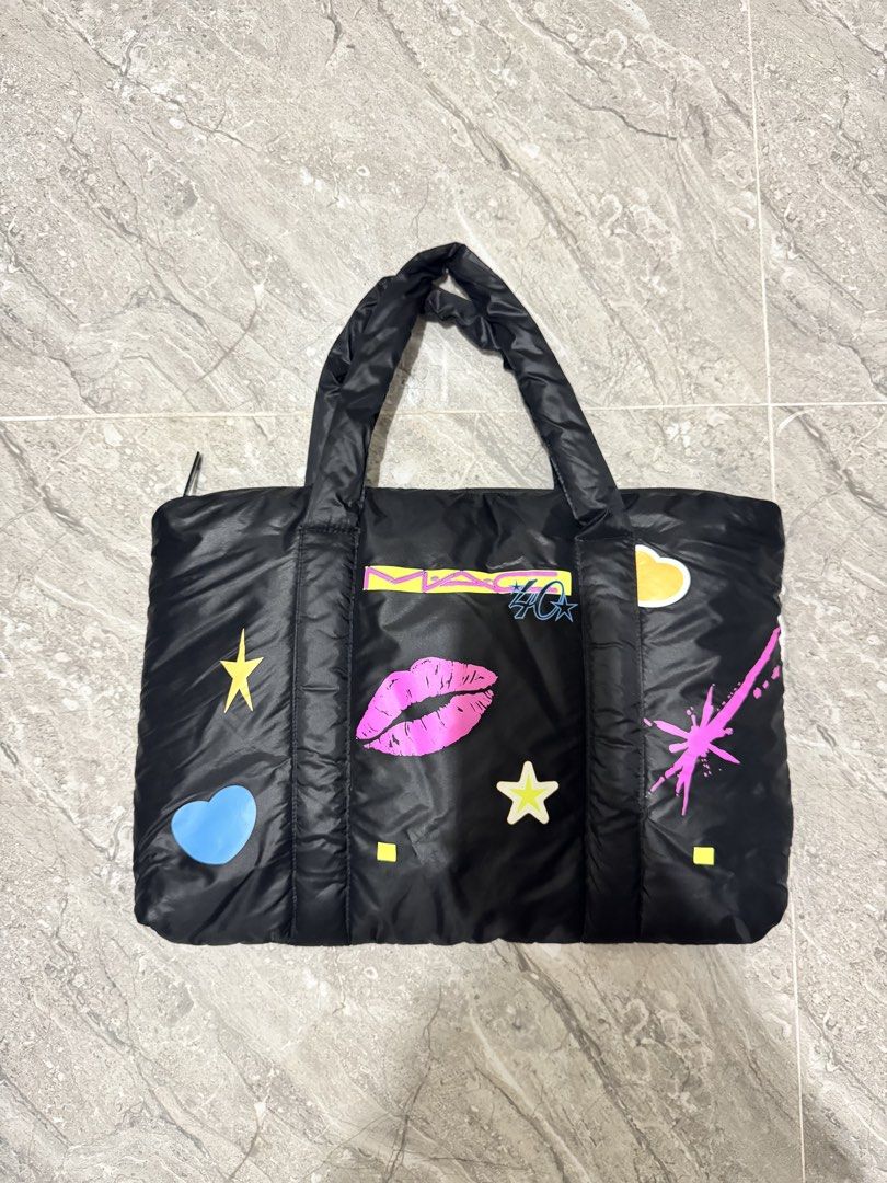 MAC Cosmetics Black Puffer Tote Bag with Graphics (Category: Tote Bags) located in Calamba. Submitted by nicalison (Listing ID 1461254647, Image 1). Description: - Chic black puffer tote bag from MAC Cosmetics. - Features playful graphics: lips, stars, and clouds. - Secure zipper closure at the top. - Comfortable, puffy handles for easy carrying. - Ideal for everyday use or travel. - Spacious interior for all your essentials..