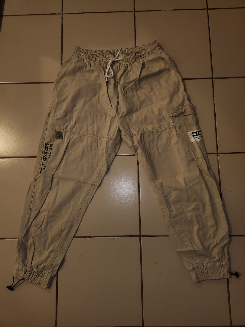 Beige Cargo Pants with Drawstring Waist (Category: Other Bottoms) located in Manila. Submitted by azzamandi339507 (Listing ID 1461366309, Image 2). Description: - Light beige cargo pants - Elastic waistband with adjustable drawstring - Cuffed ankles with adjustable toggles - Multiple functional pockets on front and sides - Subtle text details on the legs - Designed for a comfortable everyday fit - color in pictures might vary due to lighting MOP: