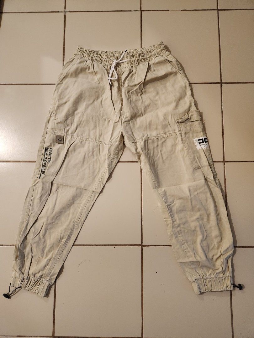 Beige Cargo Pants with Drawstring Waist (Category: Other Bottoms) located in Manila. Submitted by azzamandi339507 (Listing ID 1461366309, Image 1). Description: - Light beige cargo pants - Elastic waistband with adjustable drawstring - Cuffed ankles with adjustable toggles - Multiple functional pockets on front and sides - Subtle text details on the legs - Designed for a comfortable everyday fit - color in pictures might vary due to lighting MOP: