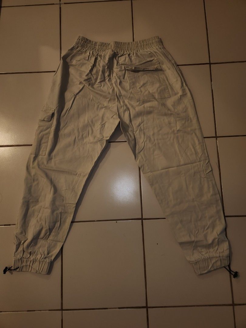 Beige Cargo Pants with Drawstring Waist (Category: Other Bottoms) located in Manila. Submitted by azzamandi339507 (Listing ID 1461366309, Image 3). Description: - Light beige cargo pants - Elastic waistband with adjustable drawstring - Cuffed ankles with adjustable toggles - Multiple functional pockets on front and sides - Subtle text details on the legs - Designed for a comfortable everyday fit - color in pictures might vary due to lighting MOP: