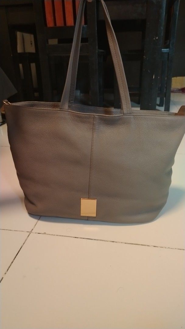couronne Grey Leather Tote Bag (Category: Tote Bags) located in Manila. Submitted by wildwind_73f77a (Listing ID 1461482599, Image 1). Description: - Grey leather tote bag by Cole Haan - Spacious interior, ideal for everyday use - Features a textured leather finish - Gold-tone accent plate on the front - Comfortable handles for easy carrying - Simple and classic design.
