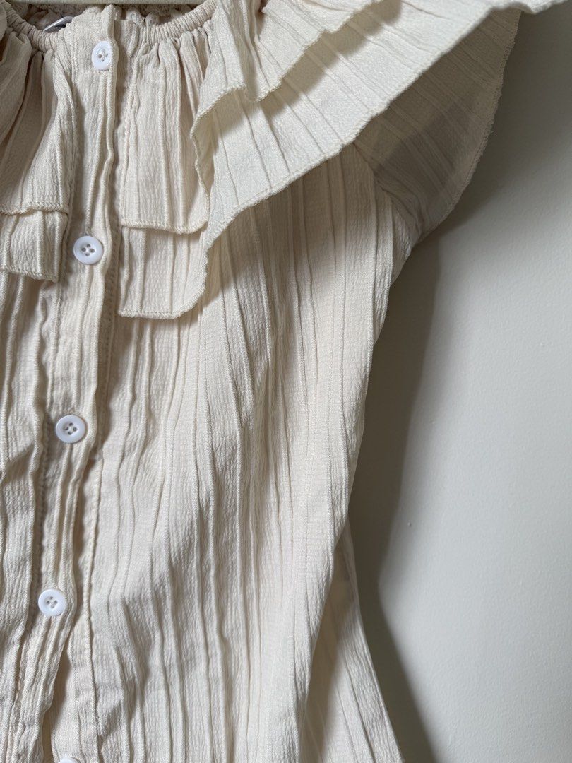 Cream Ruffled Off-Shoulder Button-Up Top (Category: Blouses) located in Pasig City. Submitted by yensyard__ (Listing ID 1461381086, Image 3). Description: - XS-S frame - Cream colored top - Ruffled neckline - Off-shoulder style - Button-up front - Textured fabric with vertical pleats - Short sleeves - Pairs well with high-waisted jeans or skirts.