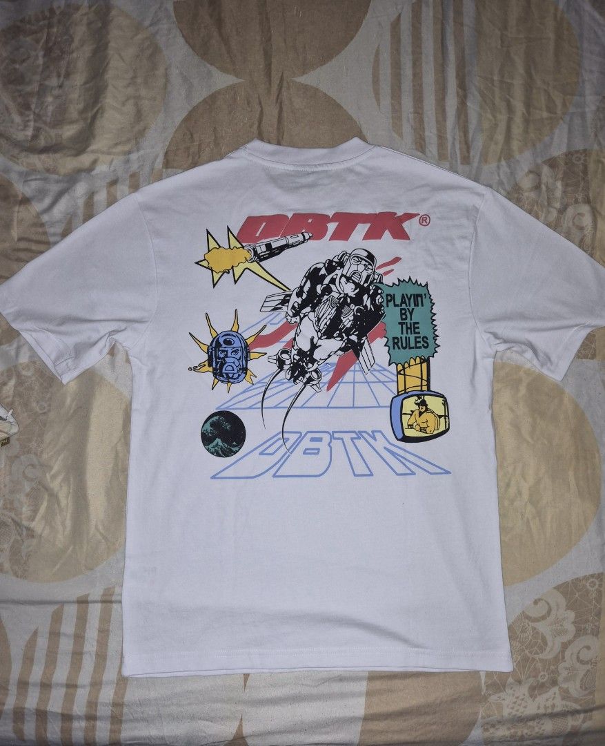 DBTK Oversized Tee White Graphic Print (Category: Tshirts & Polo Shirts ) located in Taguig. Submitted by chloe_clothingco. (Listing ID 1461369975, Image 2). Description: - White DBTK oversized t-shirt - Size: Large (L) - Unique graphic print on front and back - Designs include rocket, astronaut, and gaming themes - Comfortable fabric - Perfect for everyday casual style.