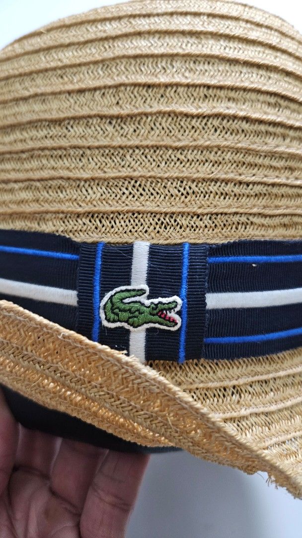 Lacoste Straw Hat with Ribbon Detail (Category: Hats & Beanies) located in Alfonso. Submitted by jbcamet (Listing ID 1461496168, Image 2). Description: - Classic Lacoste straw hat - Navy, white, and blue striped ribbon detail - Iconic embroidered Lacoste crocodile logo - Woven texture with a slightly flexible brim - Ideal for sunny outdoor activities.