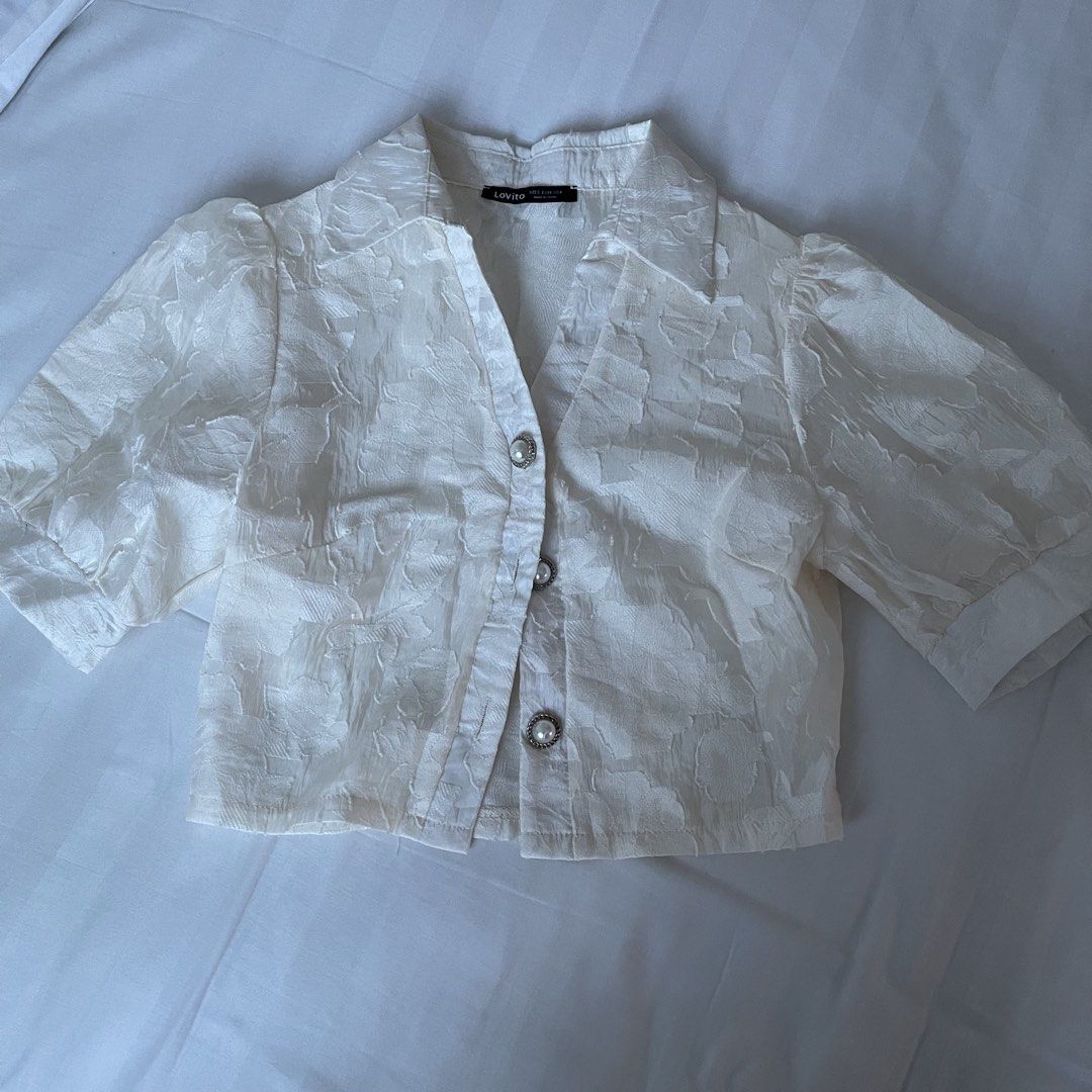 Lovito White Textured Puff Sleeve Cropped Blouse (Category: Blouses) located in Muntinlupa City. Submitted by sza1123 (Listing ID 1461415779, Image 1). Description: - White cropped blouse from Lovito - Textured fabric with a subtle floral-like pattern - Stylish puff sleeves - Elegant pearl-like buttons down the front - Classic collar neckline - Versatile for pairing with high-waisted bottoms - Effortlessly chic and easy to style.