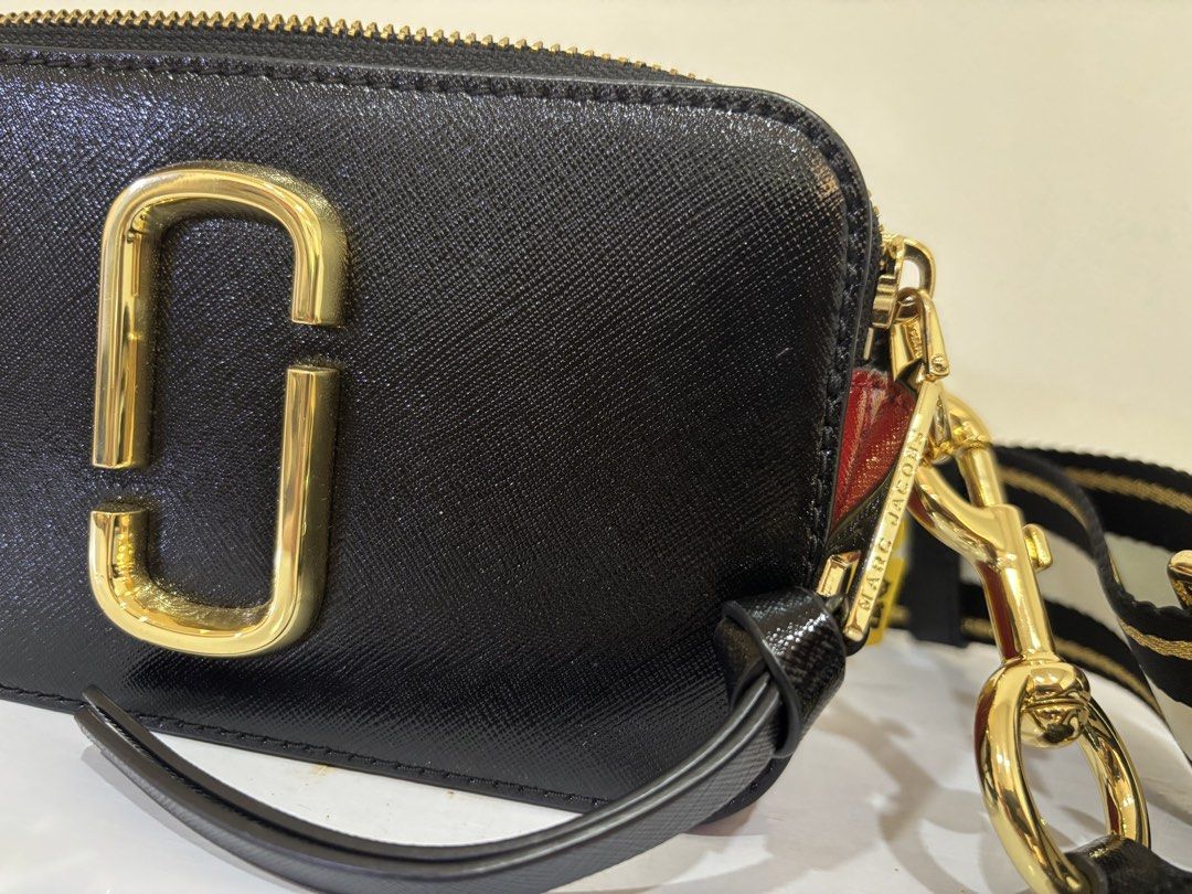 Marc Jacobs Snapshot Camera Bag Black Gold (Category: Luxury Bags & Wallets) located in Malabon City. Submitted by everythingpreloveddd (Listing ID 1461484526, Image 2). Description: - Authentic Black Marc Jacobs Snapshot bag - Signature gold MJ logo on the front - Includes a black, white, and gold striped strap - Elegant gold hardware details - Deep red side panels for a pop of color - Spacious interior for your daily essentials - Ideal for ever