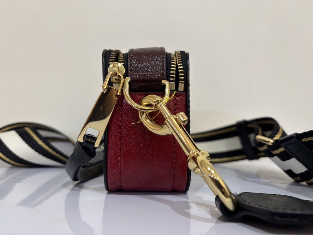 Marc Jacobs Snapshot Camera Bag Black Gold (Category: Luxury Bags & Wallets) located in Malabon City. Submitted by everythingpreloveddd (Listing ID 1461484526, Image 3). Description: - Authentic Black Marc Jacobs Snapshot bag - Signature gold MJ logo on the front - Includes a black, white, and gold striped strap - Elegant gold hardware details - Deep red side panels for a pop of color - Spacious interior for your daily essentials - Ideal for ever