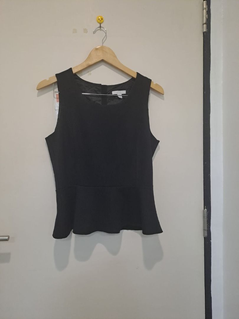 peplum black sleeveless (Category: Sleeveless) located in Mandaluyong City. Submitted by epicowl-c93c (Listing ID 1461350854, Image 1). Description: The image shows a black sleeveless peplum top hanging on a wooden coat hanger against a white door. The top features a crew-style round neckline, structured darting along the bodice for a fitted silhouette, a seam at the waist, and a characteristic flared peplum hem.This timeless, versatile piece bri