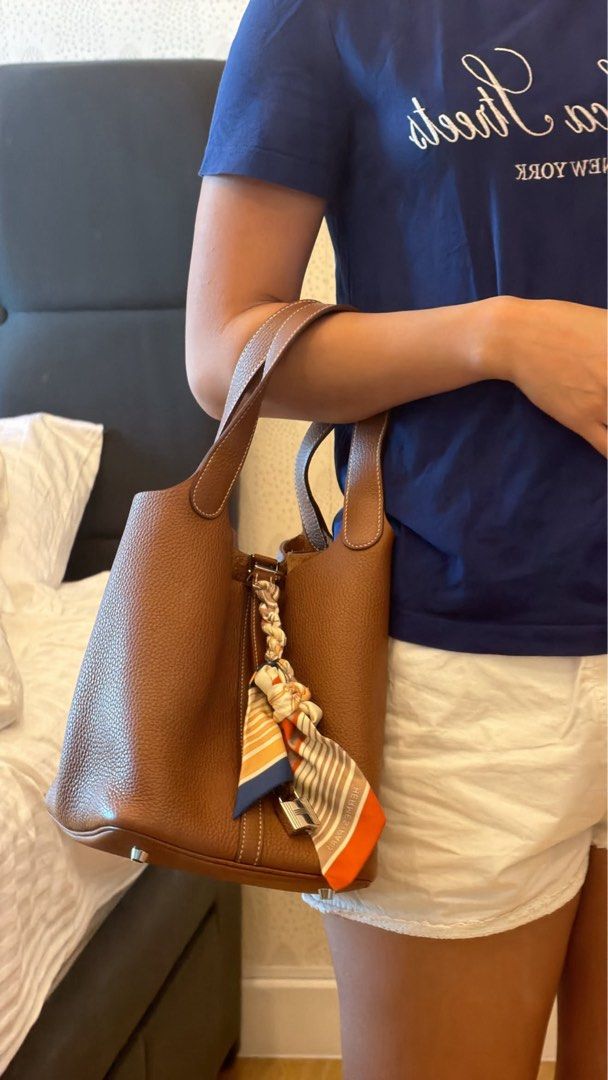 Picotin 22 gold shw w/ twilly (Category: Luxury Bags & Wallets) located in Bacoor. Submitted by ynnnaaa (Listing ID 1461497589, Image 2). Description: - Stylish brown leather bucket bag - Features a lock and key detail - Comes with a cute scarf tied to the handle - Ideal for everyday use and carrying essentials - Beautiful leather texture - Includes the original orange box.