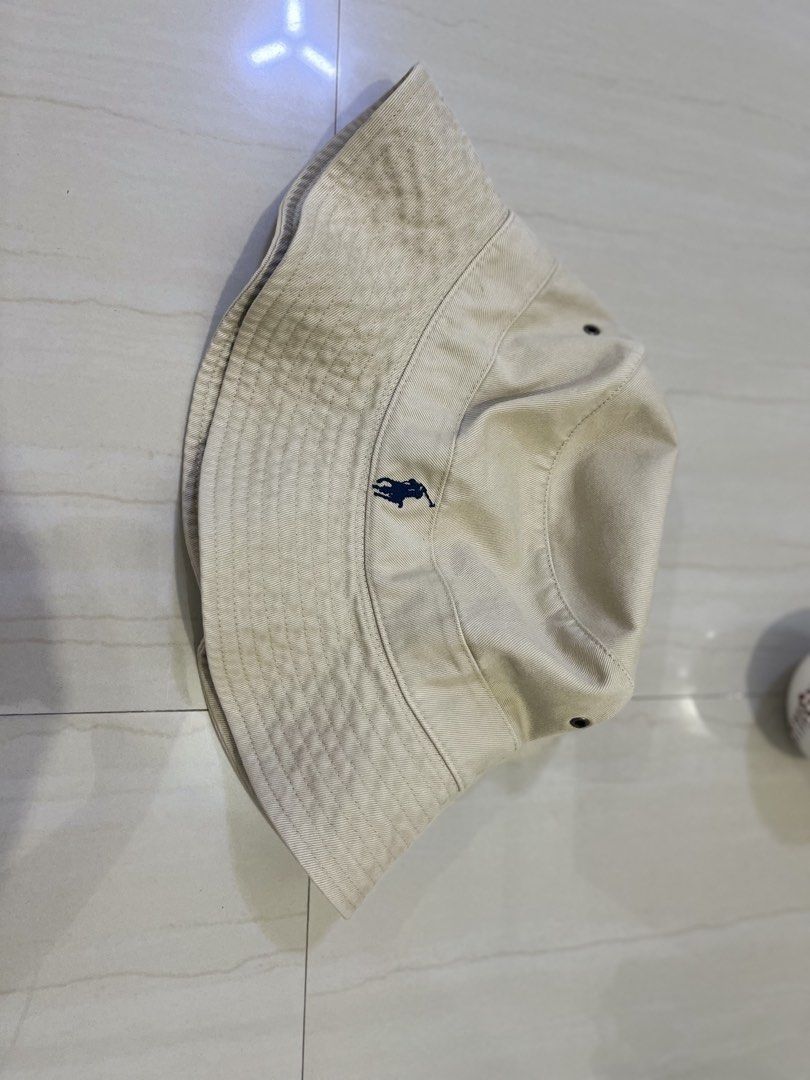 Polo Ralph Lauren Bucket Hat (Category: Caps & Hats) located in Manila. Submitted by aj_x007 (Listing ID 1461386699, Image 1). Description: - Classic beige bucket hat from Polo Ralph Lauren - Features iconic navy blue pony logo embroidered on the front - Made from durable cotton - Perfect for sunny days - Shows some signs of wear, particularly on the brim.