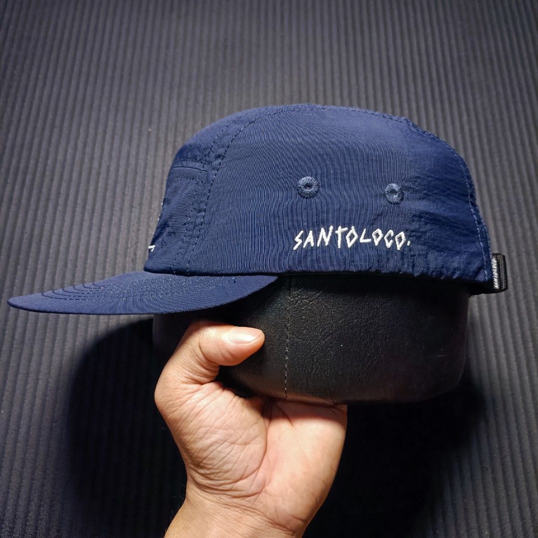 SANTOLOCO. Skate & surf apparel (Category: Caps & Hats) located in Manila. Submitted by nye.seller (Listing ID 1461494368, Image 3). Description: - Navy blue 5-panel cap - Brand: SANTOLOCO - Features a simple graphic design on the front - Adjustable strap at the back for a customized fit - Material: 100% Nylon - Ideal for everyday wear.