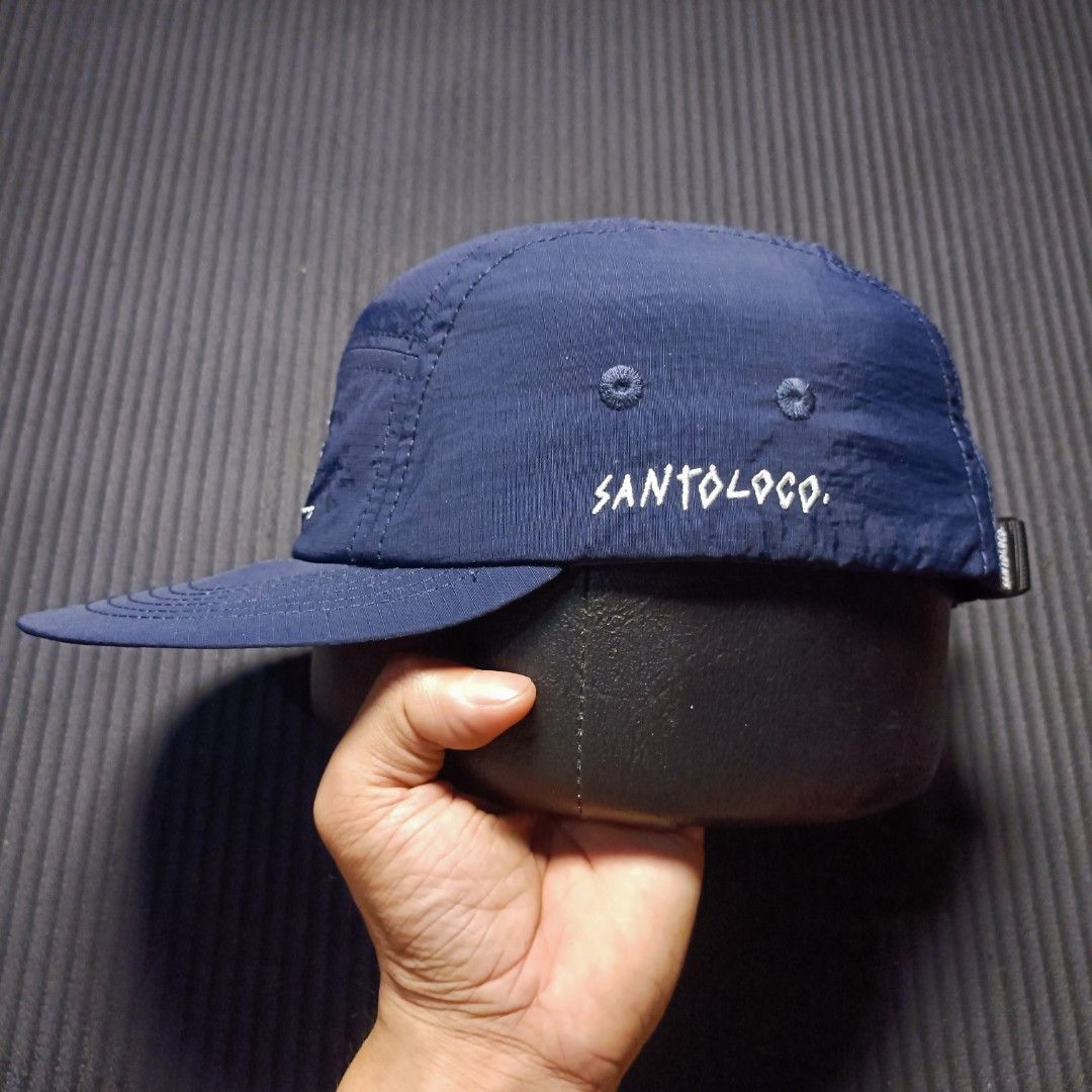 SANTOLOCO. Skate & surf apparel (Category: Caps & Hats) located in Manila. Submitted by nye.seller (Listing ID 1461494368, Image 2). Description: - Navy blue 5-panel cap - Brand: SANTOLOCO - Features a simple graphic design on the front - Adjustable strap at the back for a customized fit - Material: 100% Nylon - Ideal for everyday wear.