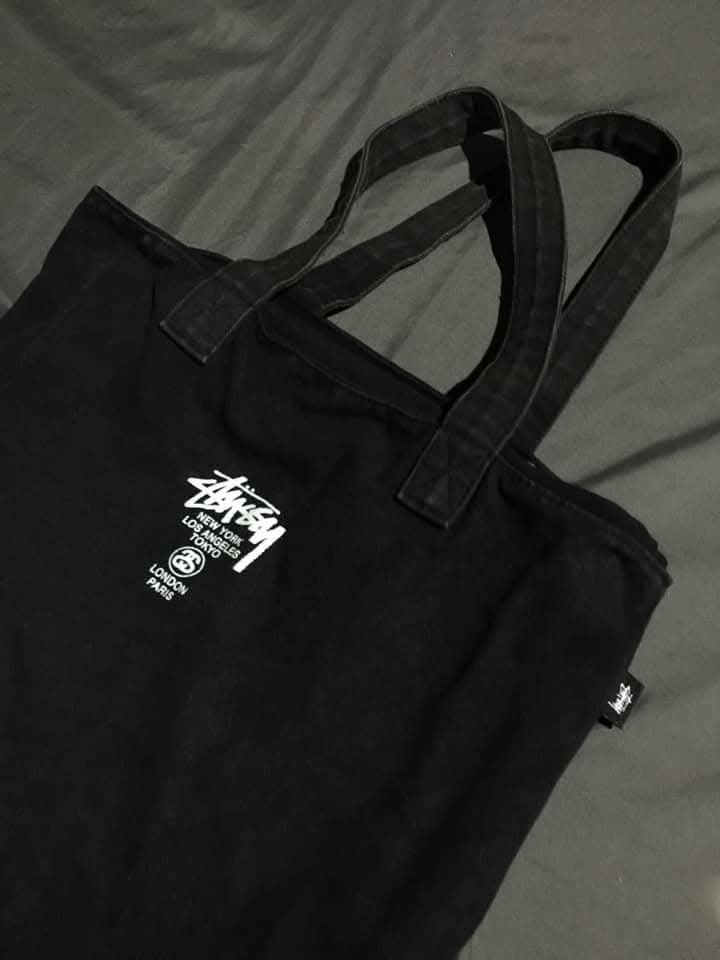 Stussy Tote Bag Black (Category: Tote Bags) located in San Antonio. Submitted by 13thrandom_ (Listing ID 1461560249, Image 2). Description: - Black Stussy tote bag - Features Stussy logo with city names (New York, Los Angeles, Tokyo, London, Paris) - Front zippered pocket - Small inner pouch - Stussy tag inside - Ideal for everyday use.