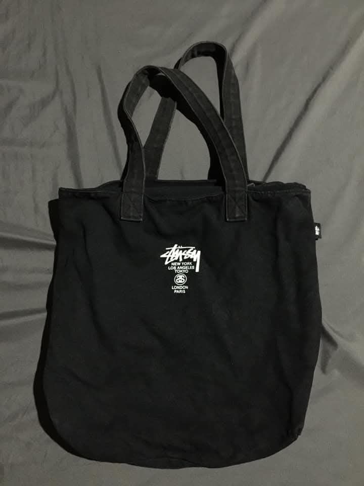 Stussy Tote Bag Black (Category: Tote Bags) located in San Antonio. Submitted by 13thrandom_ (Listing ID 1461560249, Image 1). Description: - Black Stussy tote bag - Features Stussy logo with city names (New York, Los Angeles, Tokyo, London, Paris) - Front zippered pocket - Small inner pouch - Stussy tag inside - Ideal for everyday use.
