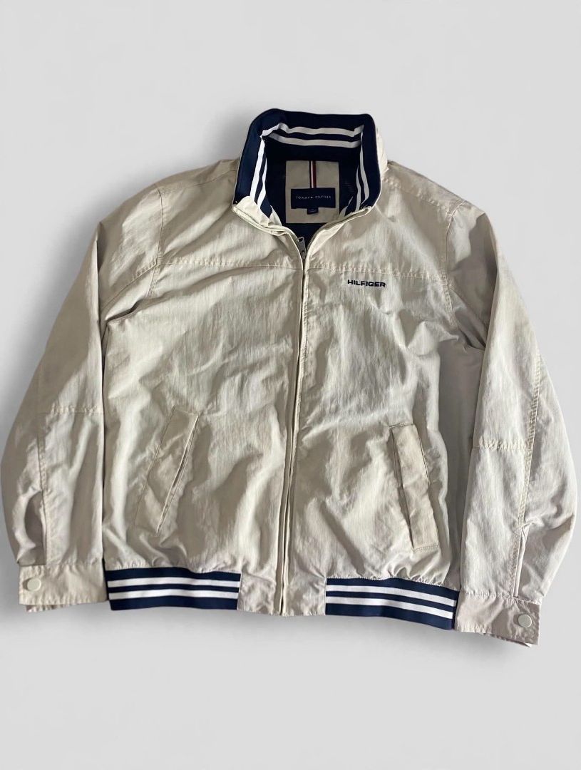 Tommy Hilfiger Beige Hooded Bomber Jacket (Category: Coats, Jackets and Outerwear) located in Bansalan. Submitted by thriftyzzz (Listing ID 1461474021, Image 1). Description: - Tommy Hilfiger beige jacket - Zip-up front with a hidden hood - Ribbed cuffs and hem with navy and white stripes - Two front pockets - Tommy Hilfiger logo on the chest - Ideal for casual wear.