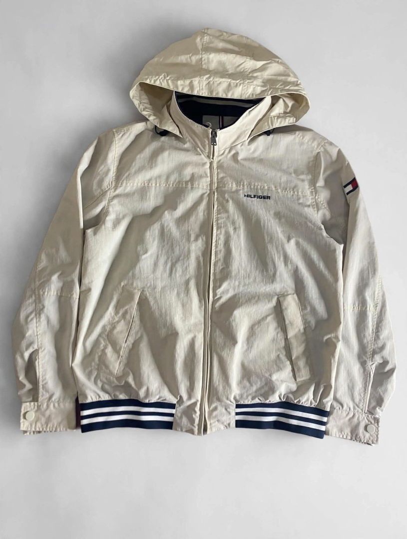 Tommy Hilfiger Beige Hooded Bomber Jacket (Category: Coats, Jackets and Outerwear) located in Bansalan. Submitted by thriftyzzz (Listing ID 1461474021, Image 2). Description: - Tommy Hilfiger beige jacket - Zip-up front with a hidden hood - Ribbed cuffs and hem with navy and white stripes - Two front pockets - Tommy Hilfiger logo on the chest - Ideal for casual wear.