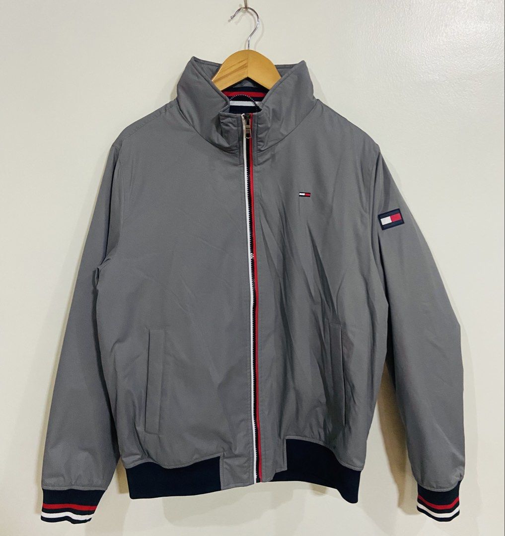 Tommy Hilfiger Grey Windbreaker Jacket Size M (Category: Coats, Jackets and Outerwear) located in Manila. Submitted by thriftnijuan08 (Listing ID 1461340196, Image 1). Description: - Grey Tommy Hilfiger jacket - Classic Tommy flag logo on chest and sleeve - Zip-up front with red and white trim - Ribbed cuffs and hem - Water and wind resistant material - Size: Medium (M) -Dimes 23/26.