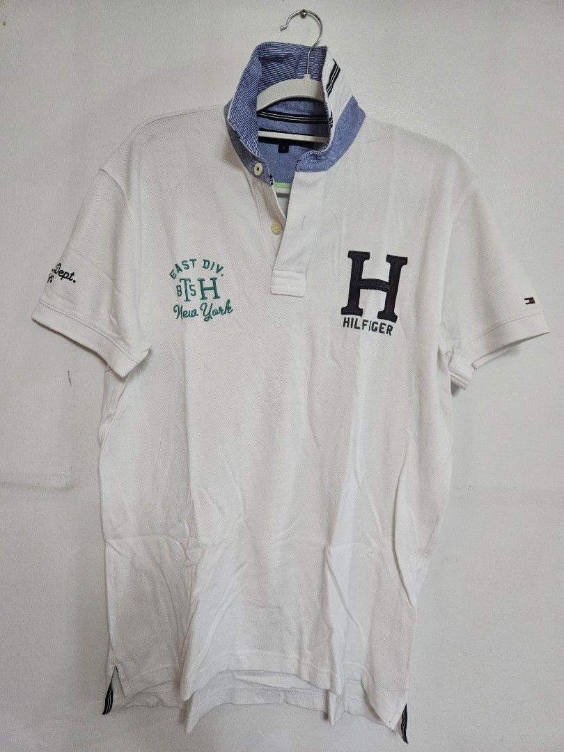 Tommy Hilfiger White Polo Shirt (Category: Tshirts & Polo Shirts ) located in Batangas. Submitted by golem08 (Listing ID 1461405556, Image 1). Description: - Classic white Tommy Hilfiger polo shirt - Large 'H' logo with 'Hilfiger' text on the chest - 'East Div 815 New York' graphic on the front - Features a classic collar and button placket - Short sleeves with ribbed cuffs - Ideal for casual everyday wear.