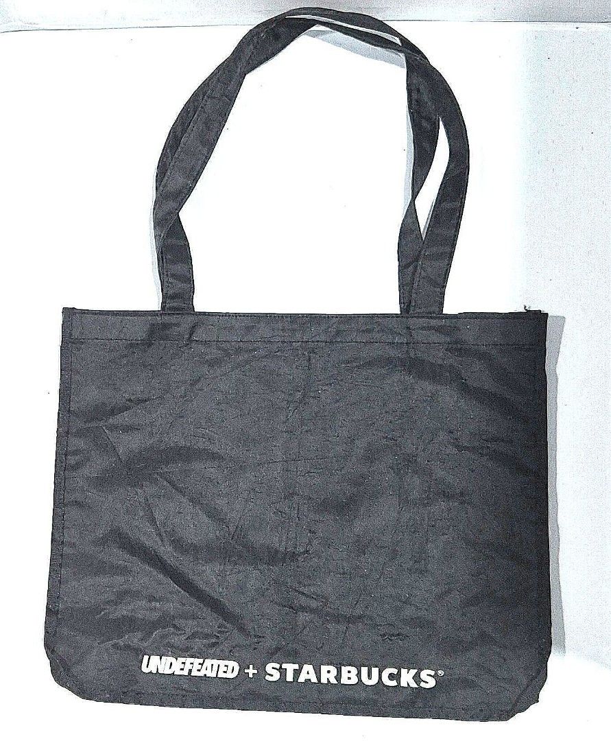 Undefeated x Starbucks Black Tote Bag (Category: Tote Bags) located in Antipolo. Submitted by saribymonica (Listing ID 1461465849, Image 2). Description: - Authentic Undefeated x Starbucks collaboration black tote bag. - Features the iconic bright yellow Undefeated logo on one side. - Showcases the Undefeated + Starbucks branding on the opposite side. - Includes a convenient small pocket inside. - Ideal for everyday use and carrying your essentia