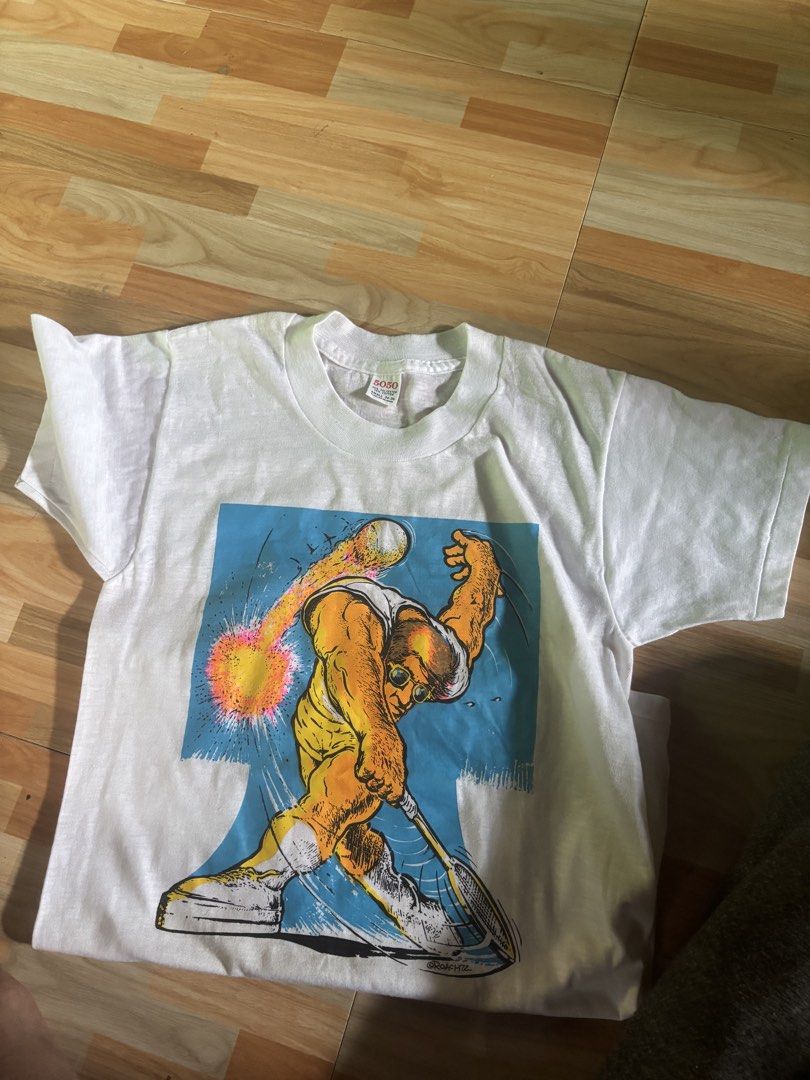 Vintage Roach 72 Graphic T-Shirt (Category: Tshirts & Polo Shirts ) located in Tubigon. Submitted by wawiesunbe75372 (Listing ID 1461457244, Image 1). Description: - Vintage white t-shirt - Cool graphic print: Muscular figure playing tennis, signed 'Roach '72' - Size: Small - Material: 50% Polyester, 50% Cotton - Origin: Made in USA - Ideal for collectors or fans of retro graphics.