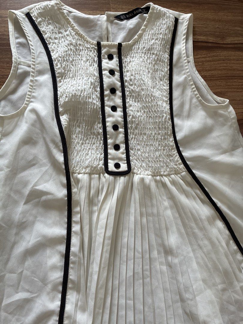 Zara Basic White Pleated Smocked Button Down Sleeveless Top XS (Category: Sleeveless) located in Pasig City. Submitted by slr1949 (Listing ID 1461409989, Image 3). Description: - White sleeveless top from Zara Basic - Smocked bodice with black button accents - Pleated design on the lower part - Black trim along neckline and down the front - Versatile for casual or dressed-up looks.