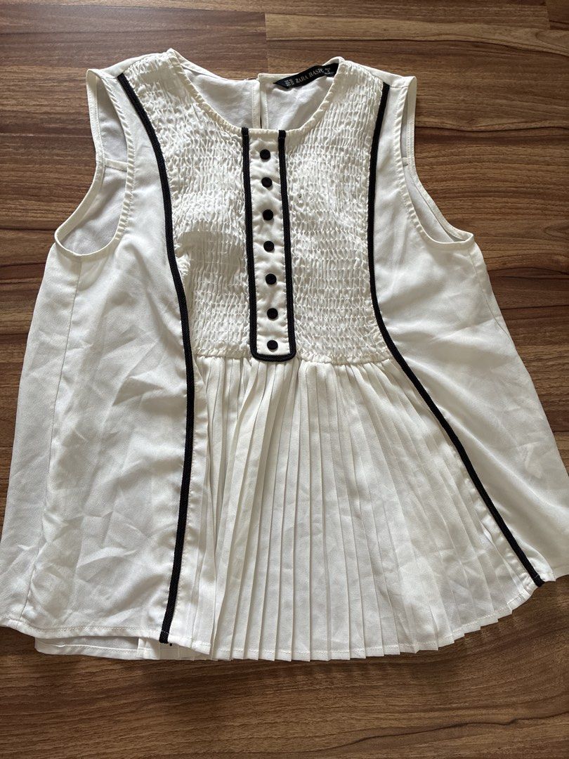 Zara Basic White Pleated Smocked Button Down Sleeveless Top XS (Category: Sleeveless) located in Pasig City. Submitted by slr1949 (Listing ID 1461409989, Image 1). Description: - White sleeveless top from Zara Basic - Smocked bodice with black button accents - Pleated design on the lower part - Black trim along neckline and down the front - Versatile for casual or dressed-up looks.