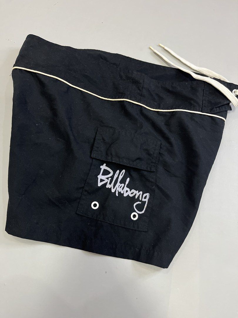 Billabong Black Board Shorts (Category: Swim Trunks & Board Shorts) located in Mabalacat. Submitted by aas_thriftfings (Listing ID 1461589727, Image 3). Description: - Brand: Billabong - Size: W34 L13 - Color: Black with red and white graffiti-style logo - Features: Drawstring waist, back pocket with button closure - Material: 100% Polyester - Origin: Made in Thailand.