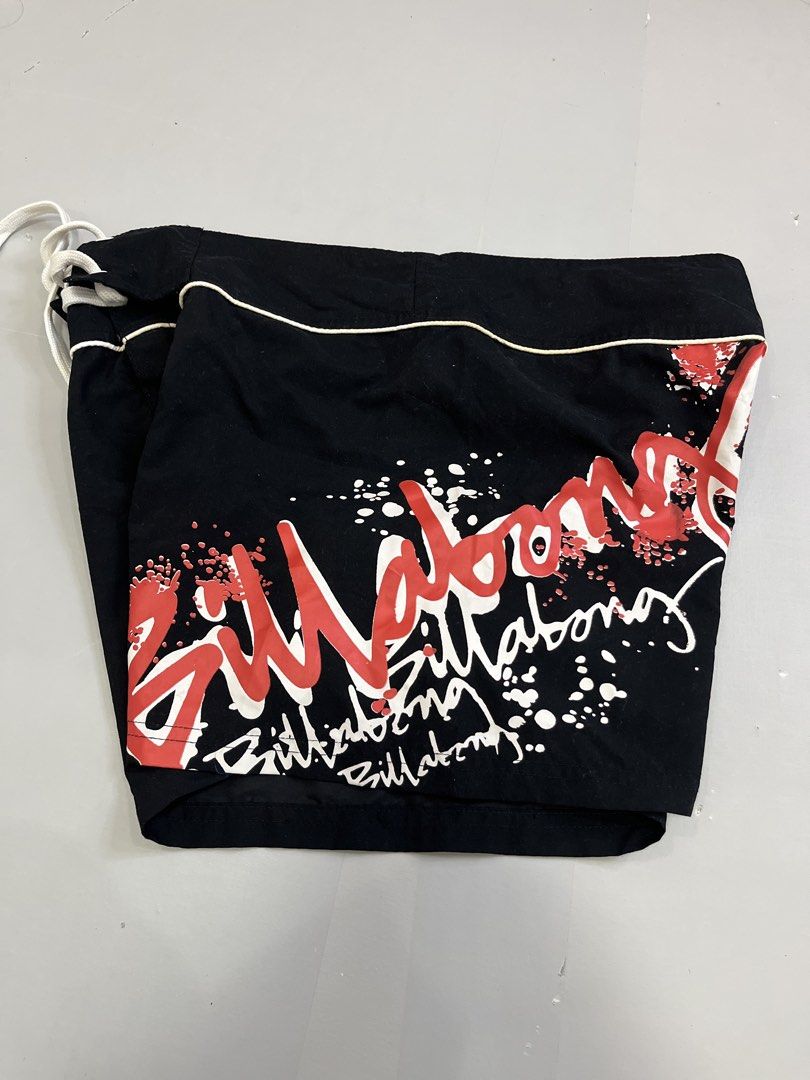Billabong Black Board Shorts (Category: Swim Trunks & Board Shorts) located in Mabalacat. Submitted by aas_thriftfings (Listing ID 1461589727, Image 2). Description: - Brand: Billabong - Size: W34 L13 - Color: Black with red and white graffiti-style logo - Features: Drawstring waist, back pocket with button closure - Material: 100% Polyester - Origin: Made in Thailand.