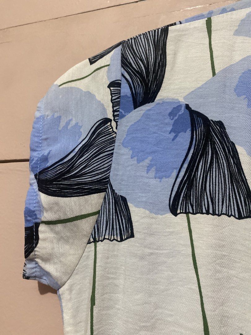 Blue Floral Button-Up Short Sleeve Top (Category: Blouses) located in Manila. Submitted by angelaay143 (Listing ID 1461775987, Image 3). Description: - White top with blue and black floral print - Short sleeves with gathered detail - Button-up front with collar - Lightweight fabric, ideal for warm weather - Versatile for casual or dressed-up looks - Needs laundry atored too long at the cabinet.