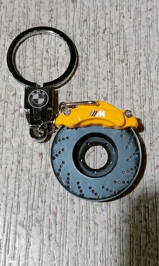 Bmw keychain (Category: Other Stationery & Craft) located in Quezon City. Submitted by Bernz (Listing ID 1461572760, Image 1). Description: This image displays a custom BMW M-Performance brake disc and caliper keychain. The piece features a miniature drilled metal brake rotor attached to a yellow brake caliper stamped with the iconic BMW ///M logo, paired with a standard chrome key ring and a BMW roundel logo base plate..