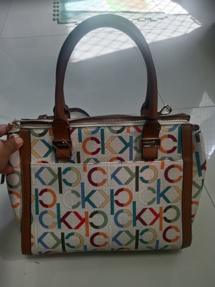 Calvin Klein Monogrammed Satchel Handbag (Category: Shoulder Bags) located in Manila. Submitted by wildwind_73f77a (Listing ID 1461640026, Image 2). Description: - Cute Calvin Klein satchel bag - All-over CK monogram print - Brown leather trim and handles - Zipper closure - Front pockets - Original tag still attached - Measures approximately 13 inches wide.