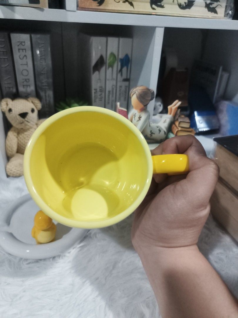 Cute Yellow Dinosaur Mug with Saucer (Category: Coffee & Tea Tableware) located in Cabuyao City. Submitted by chaptersandwonders143 (Listing ID 1461714857, Image 3). Description: - Adorable yellow mug with a charming penguin figure at the base. - Comes with a matching white saucer. - Features a bright yellow heart-shaped handle. - Ideal for enjoying your morning coffee or tea. - Fun and quirky design, perfect for gifting or personal collection..
