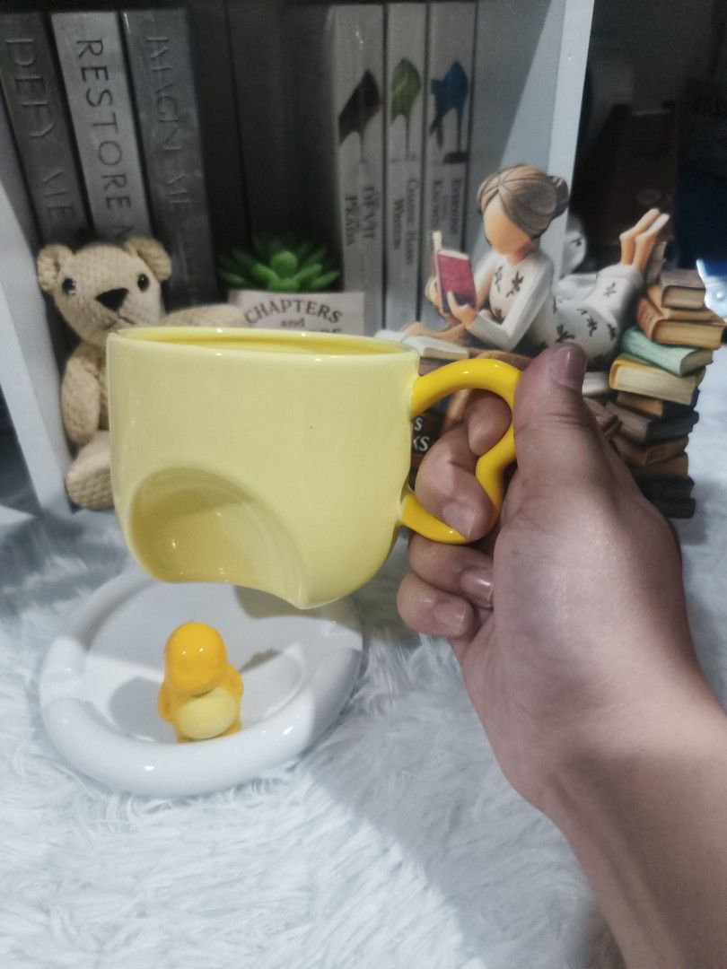 Cute Yellow Dinosaur Mug with Saucer (Category: Coffee & Tea Tableware) located in Cabuyao City. Submitted by chaptersandwonders143 (Listing ID 1461714857, Image 2). Description: - Adorable yellow mug with a charming penguin figure at the base. - Comes with a matching white saucer. - Features a bright yellow heart-shaped handle. - Ideal for enjoying your morning coffee or tea. - Fun and quirky design, perfect for gifting or personal collection..