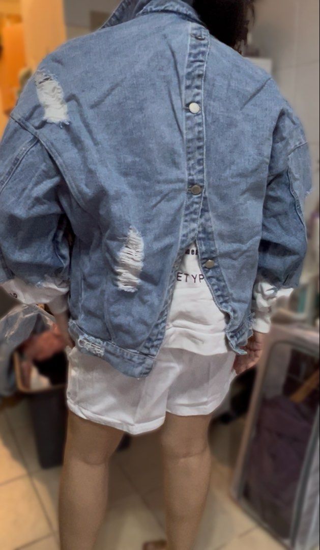 Distressed Denim Jacket with White Sleeve Inserts (Category: Coats, Jackets and Outerwear) located in Surigao. Submitted by boonz71_1971 (Listing ID 1461709345, Image 3). Description: Declutter Sale for women - Width 24” Length 20” - Oversized distressed denim jacket - Features ripped details on front and back - White long sleeves with black text print at cuffs - Unique button closure at the back - Ideal for layering - Pairs well with shorts or j