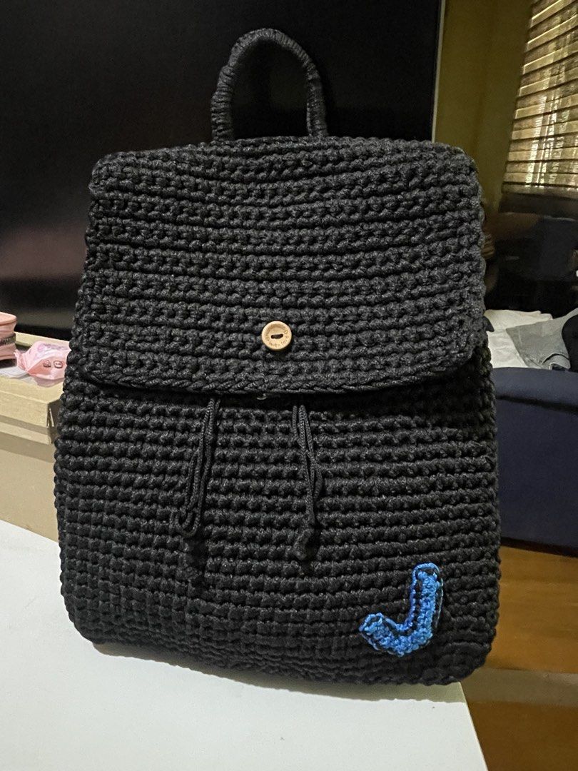 Handmade Black Crocheted Backpack (Category: Backpacks) located in Santa Cruz. Submitted by lilpurpleseven (Listing ID 1461573733, Image 1). Description: - Handmade black crocheted backpack - Secure drawstring closure with a flap and wooden button - Unique blue crocheted initial 'J' on the front - Adjustable straps for comfortable wear - Ideal for everyday use or as a thoughtful gift.
