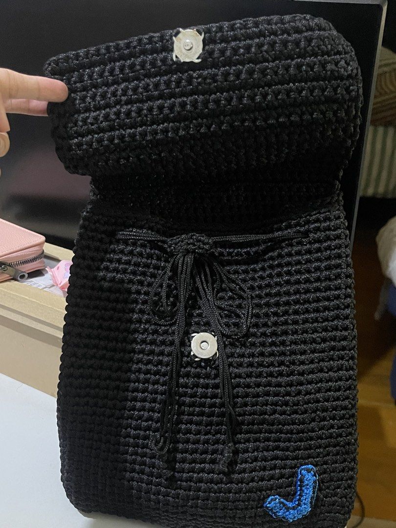 Handmade Black Crocheted Backpack (Category: Backpacks) located in Santa Cruz. Submitted by lilpurpleseven (Listing ID 1461573733, Image 2). Description: - Handmade black crocheted backpack - Secure drawstring closure with a flap and wooden button - Unique blue crocheted initial 'J' on the front - Adjustable straps for comfortable wear - Ideal for everyday use or as a thoughtful gift.