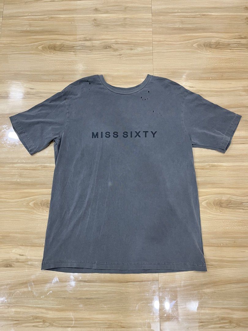 Miss Sixty T-Shirt (Category: Shirts) located in Angeles City. Submitted by thriftsij (Listing ID 1461765534, Image 1). Description: - Grey Miss Sixty t-shirt with back design - Features the iconic Miss Sixty logo on the front - Unique floral-like embellishments with pink and white details on the back - Minor distressed holes near the neckline add character - Size: EUR XS - Perfect statement piece to elevate your style.