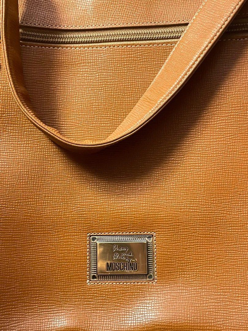 Moschino Leather Handbag with Heart Charm (Category: Luxury Bags & Wallets) located in Quezon City. Submitted by hadescloset (Listing ID 1461690877, Image 2). Description: - Authentic Moschino brown leather handbag - Features a gold-tone heart charm with 'M' initial - Top handle and detachable shoulder strap - Textured exterior finish - Secure zipper closure at the top - Comes with original dust bag - Ideal for everyday wear and adding a touch of